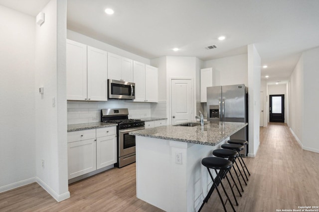 kitchen with light stone counters, stainless steel appliances, sink, white cabinets, and an island with sink