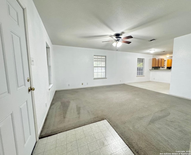 unfurnished living room with ceiling fan, light colored carpet, and a textured ceiling