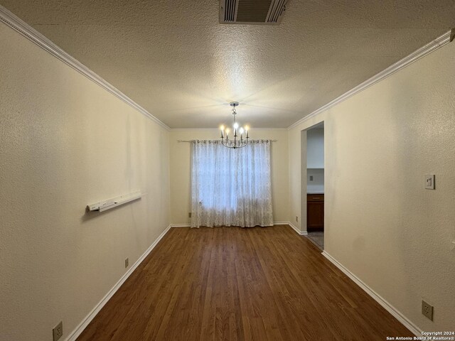 unfurnished dining area featuring a textured ceiling, crown molding, dark hardwood / wood-style floors, and a notable chandelier