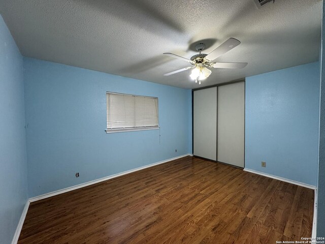 unfurnished bedroom with a textured ceiling, a closet, ceiling fan, and dark wood-type flooring