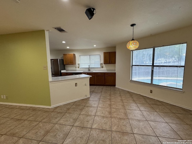 kitchen with stainless steel refrigerator, sink, light tile patterned floors, and hanging light fixtures