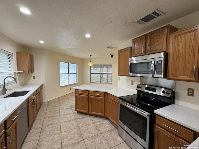 kitchen featuring kitchen peninsula, appliances with stainless steel finishes, sink, light tile patterned floors, and decorative light fixtures