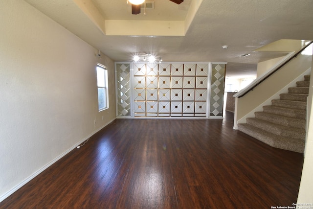 unfurnished living room featuring a textured ceiling, ceiling fan, a tray ceiling, and dark hardwood / wood-style floors