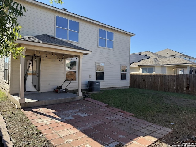 rear view of property with central air condition unit, a lawn, and a patio