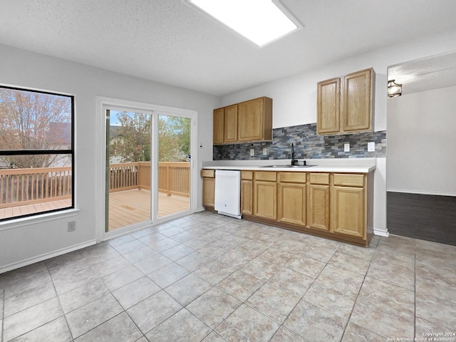 kitchen with dishwasher, backsplash, sink, light tile patterned floors, and a textured ceiling