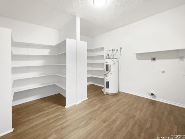 interior space featuring electric dryer hookup, water heater, wood-type flooring, and a textured ceiling