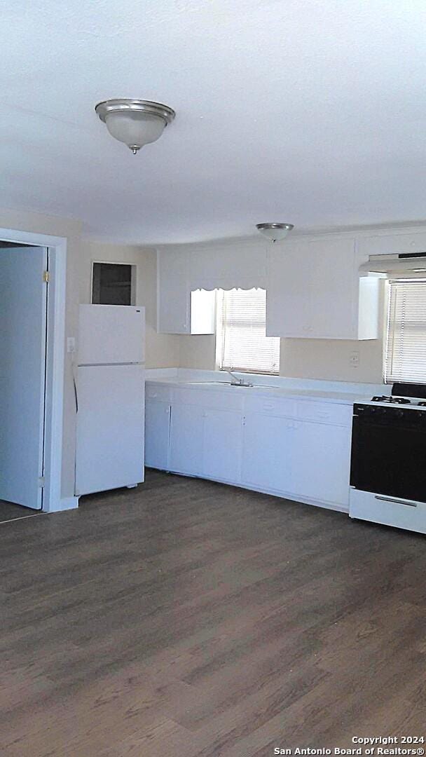 kitchen featuring stove, dark wood-type flooring, exhaust hood, white fridge, and white cabinetry