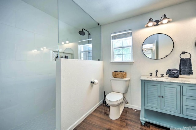 bathroom featuring a tile shower, hardwood / wood-style floors, vanity, and toilet