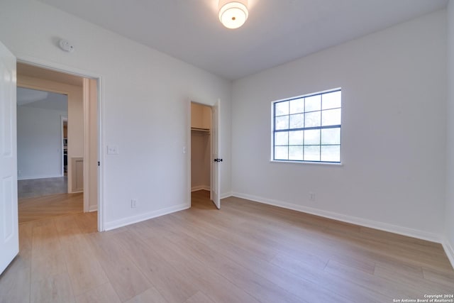 unfurnished bedroom featuring a walk in closet, a closet, and light hardwood / wood-style floors