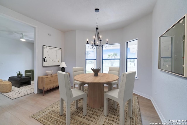 dining space with ceiling fan with notable chandelier and light hardwood / wood-style flooring