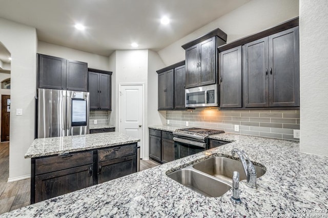 kitchen featuring wood-type flooring, backsplash, stainless steel appliances, and light stone counters