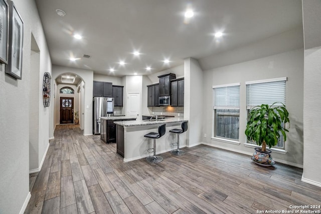 kitchen featuring backsplash, a breakfast bar area, dark hardwood / wood-style floors, light stone countertops, and stainless steel appliances