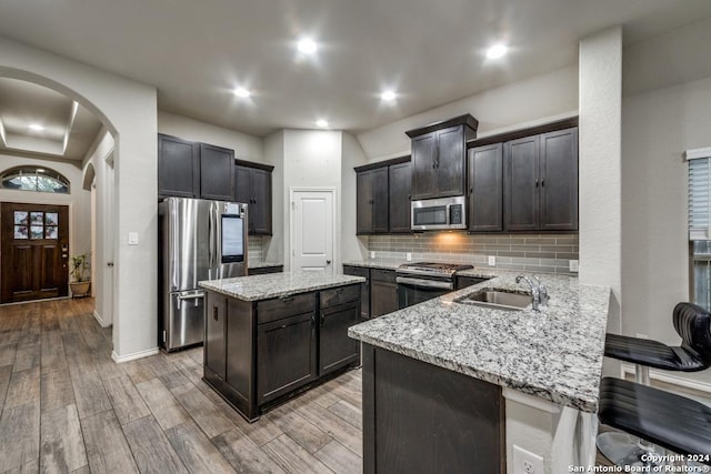 kitchen featuring decorative backsplash, light wood-type flooring, stainless steel appliances, sink, and a kitchen island