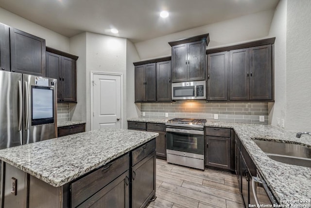 kitchen with stainless steel appliances, light stone counters, light hardwood / wood-style floors, and sink