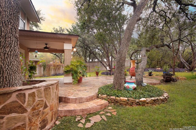 yard at dusk with ceiling fan and a patio