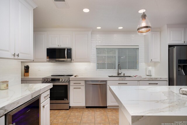 kitchen with stainless steel appliances, beverage cooler, sink, white cabinetry, and hanging light fixtures