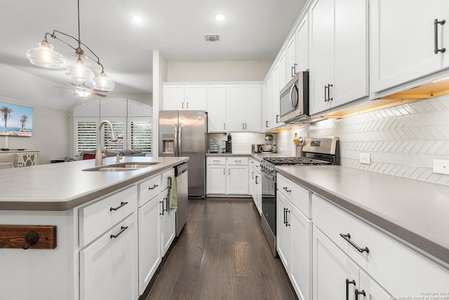 kitchen with appliances with stainless steel finishes, sink, pendant lighting, white cabinetry, and lofted ceiling