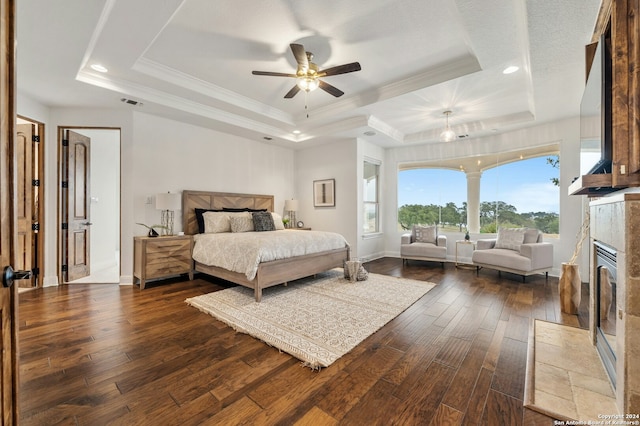 bedroom with ornamental molding, a tray ceiling, ceiling fan, dark wood-type flooring, and a fireplace