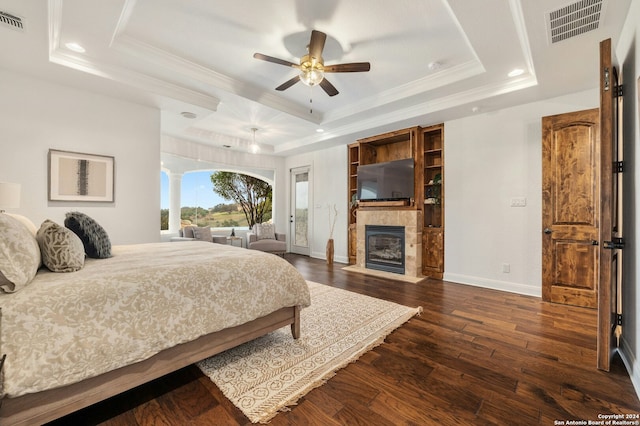 bedroom with dark hardwood / wood-style flooring, ceiling fan, a raised ceiling, and a tiled fireplace