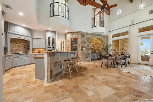 kitchen with backsplash, gray cabinetry, ceiling fan, a high ceiling, and a breakfast bar area