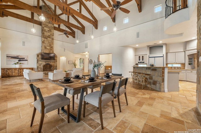 dining area featuring ceiling fan, beam ceiling, a stone fireplace, and high vaulted ceiling