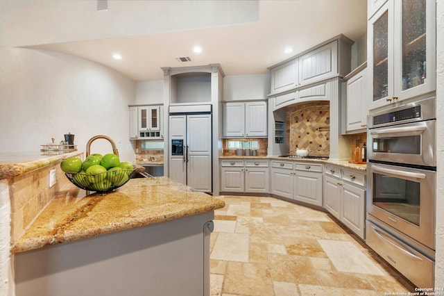 kitchen featuring tasteful backsplash, gray cabinetry, light stone countertops, and stainless steel appliances