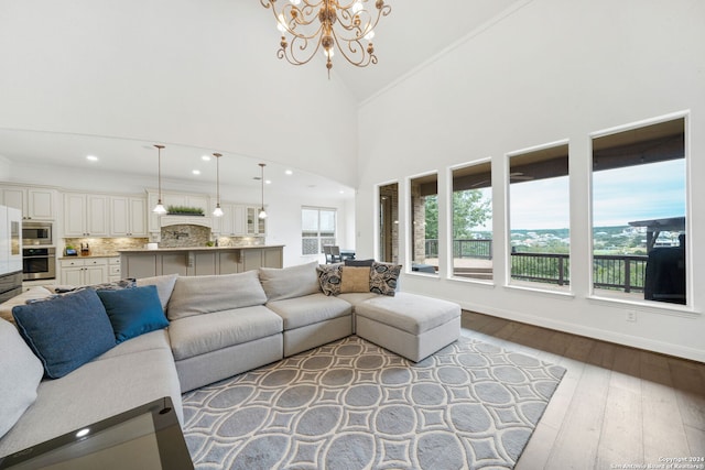 living room featuring crown molding, high vaulted ceiling, light hardwood / wood-style floors, and a notable chandelier