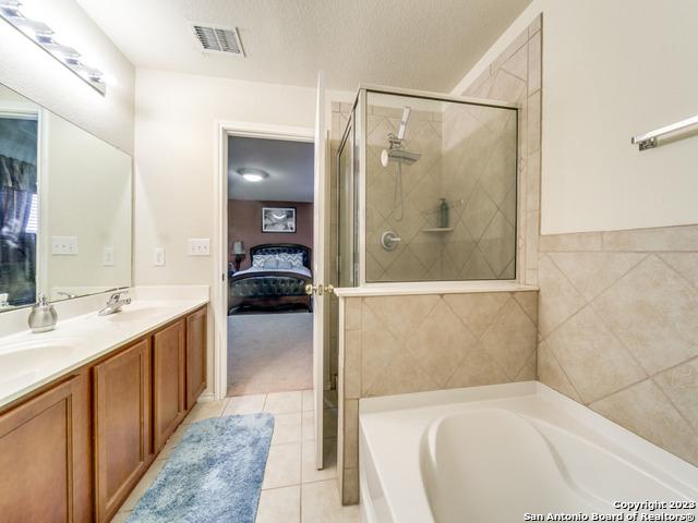 bathroom featuring plus walk in shower, tile patterned floors, a textured ceiling, vanity, and tile walls