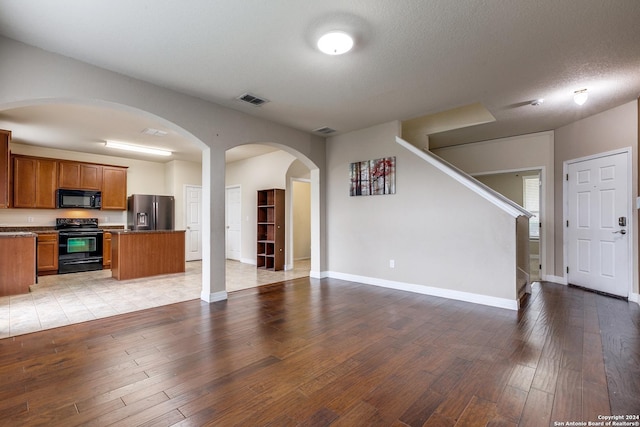 kitchen featuring a kitchen island, black appliances, a textured ceiling, and light hardwood / wood-style floors