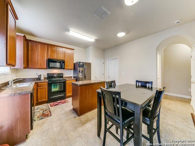 kitchen with sink, a kitchen island, dark stone countertops, and black appliances