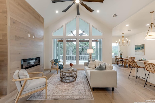 living room featuring a tile fireplace, ceiling fan with notable chandelier, high vaulted ceiling, and light hardwood / wood-style flooring