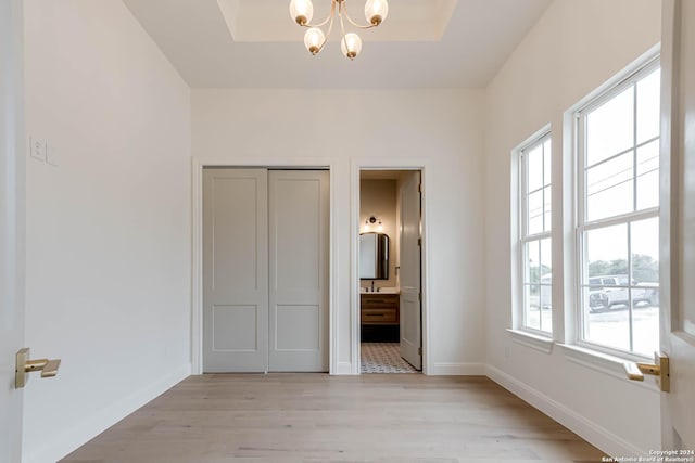 unfurnished bedroom with ensuite bathroom, an inviting chandelier, a closet, and light hardwood / wood-style flooring