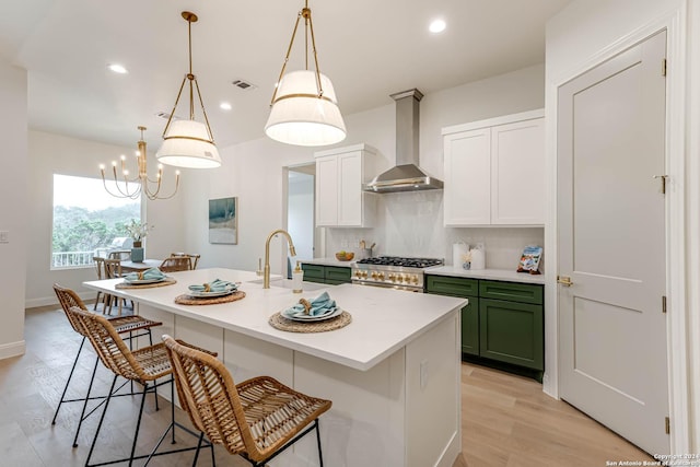 kitchen with high end range, sink, wall chimney range hood, decorative light fixtures, and an island with sink