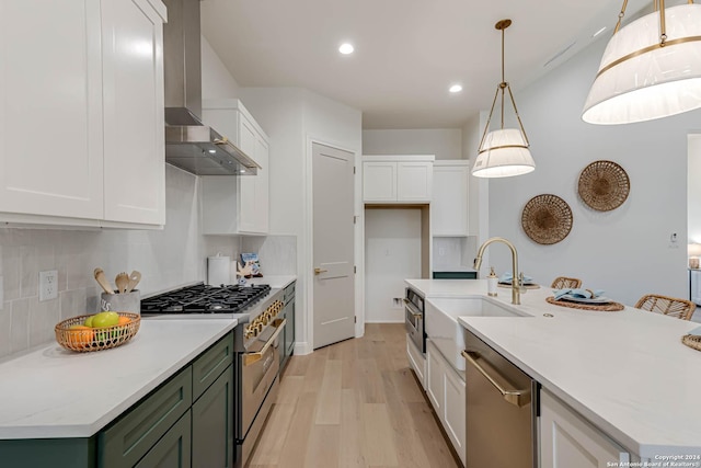 kitchen with hanging light fixtures, wall chimney range hood, light hardwood / wood-style flooring, white cabinets, and appliances with stainless steel finishes