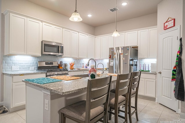 kitchen with stainless steel appliances, white cabinetry, and an island with sink