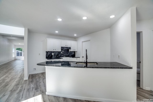 kitchen featuring kitchen peninsula, sink, dark stone countertops, light hardwood / wood-style floors, and white cabinetry