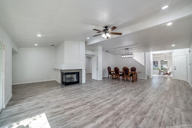 living room with ceiling fan with notable chandelier, light wood-type flooring, and a tiled fireplace