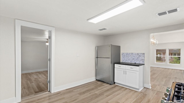 kitchen featuring white cabinetry, backsplash, stainless steel fridge, stove, and light wood-type flooring