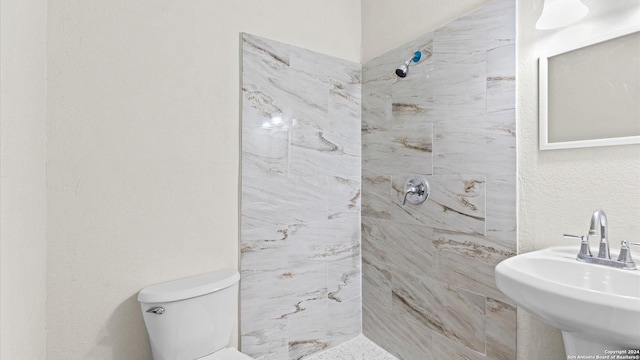 bathroom featuring toilet, a tile shower, and sink