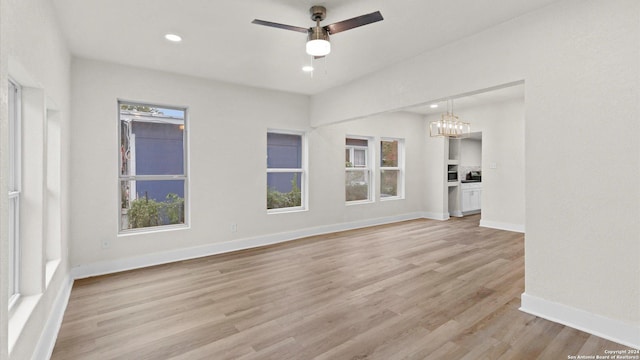 unfurnished living room with ceiling fan with notable chandelier and light wood-type flooring