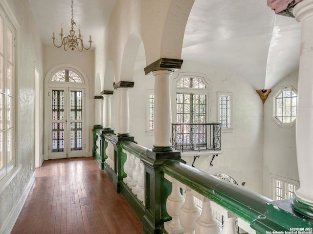 hallway with french doors, an inviting chandelier, decorative columns, wood-type flooring, and lofted ceiling