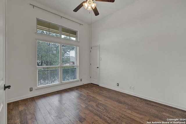 empty room with a high ceiling, dark wood-type flooring, ceiling fan, and a healthy amount of sunlight