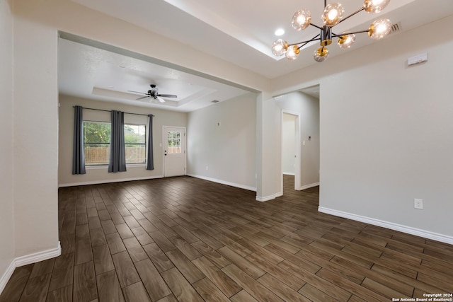 empty room with ceiling fan with notable chandelier, dark hardwood / wood-style flooring, and a tray ceiling