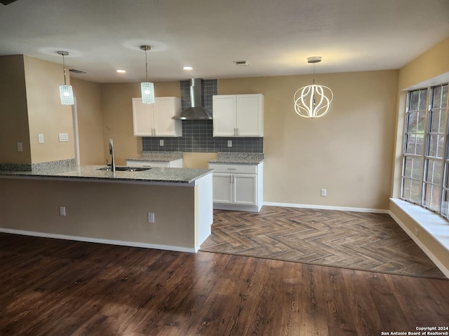 kitchen featuring light stone countertops, sink, wall chimney range hood, pendant lighting, and white cabinetry