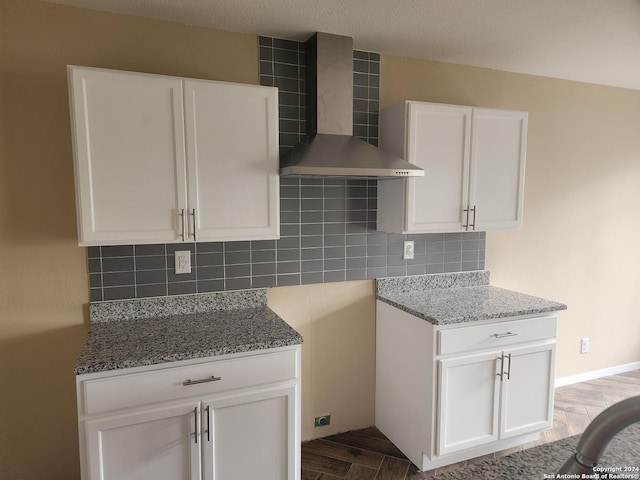 kitchen with decorative backsplash, white cabinetry, hardwood / wood-style floors, and wall chimney range hood