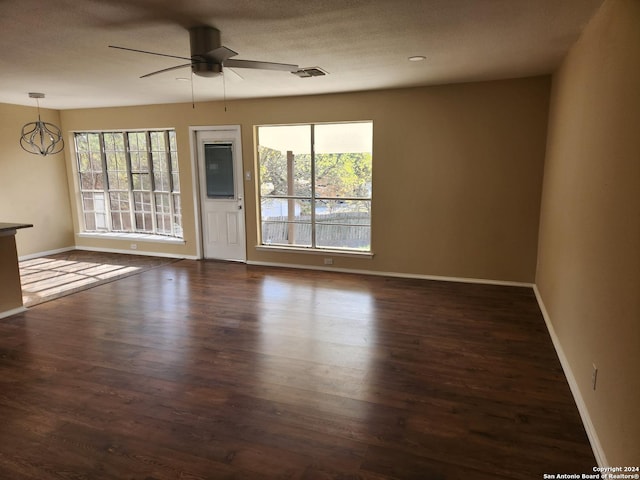 unfurnished room with ceiling fan with notable chandelier, a textured ceiling, dark hardwood / wood-style flooring, and a wealth of natural light