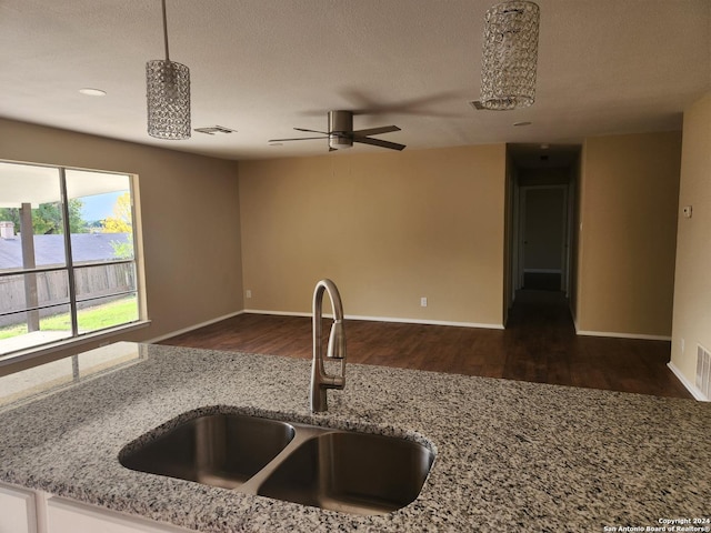 kitchen featuring sink, light stone countertops, a textured ceiling, decorative light fixtures, and dark hardwood / wood-style flooring