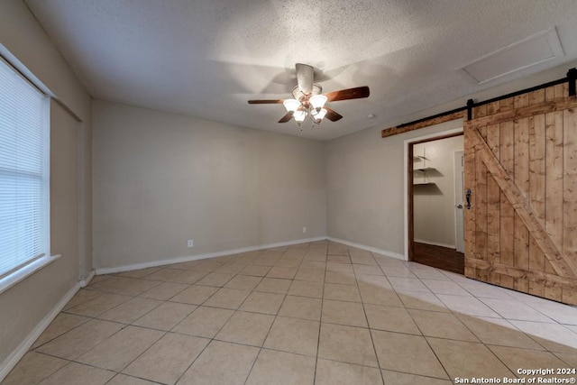 tiled empty room featuring ceiling fan, a barn door, and a textured ceiling