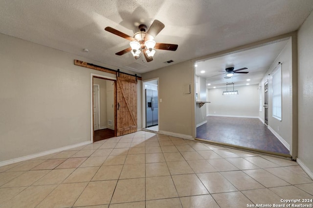 tiled spare room featuring a textured ceiling, a barn door, and ceiling fan