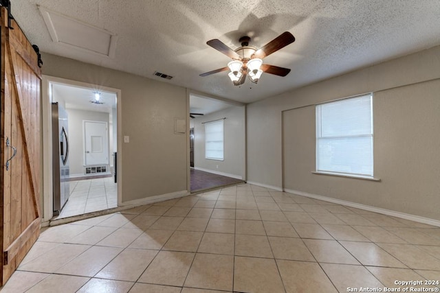 tiled empty room with ceiling fan, a barn door, a textured ceiling, and wooden walls